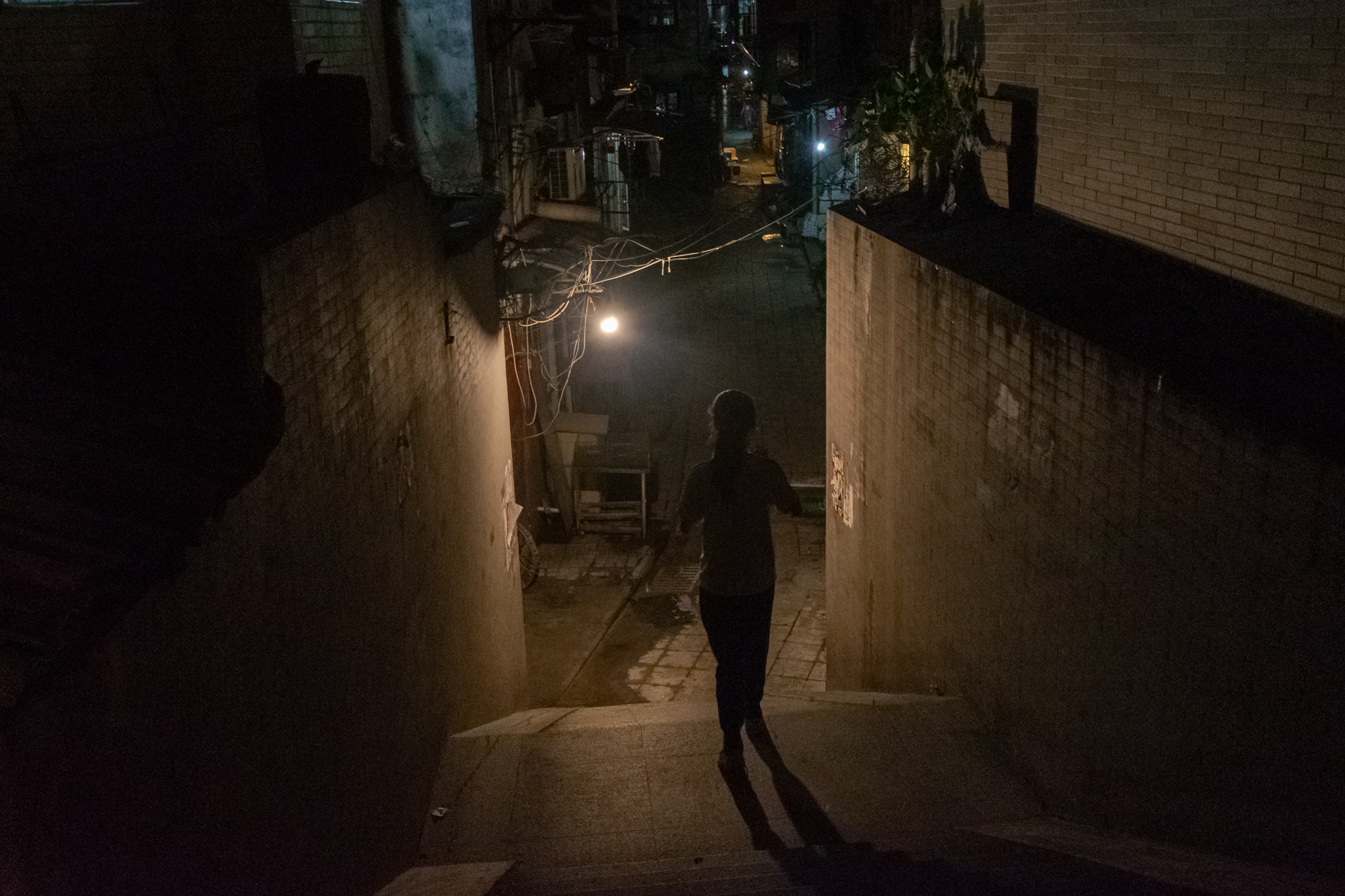 Solitary figure descends stairs into a lit alley at night, Guangzhou China