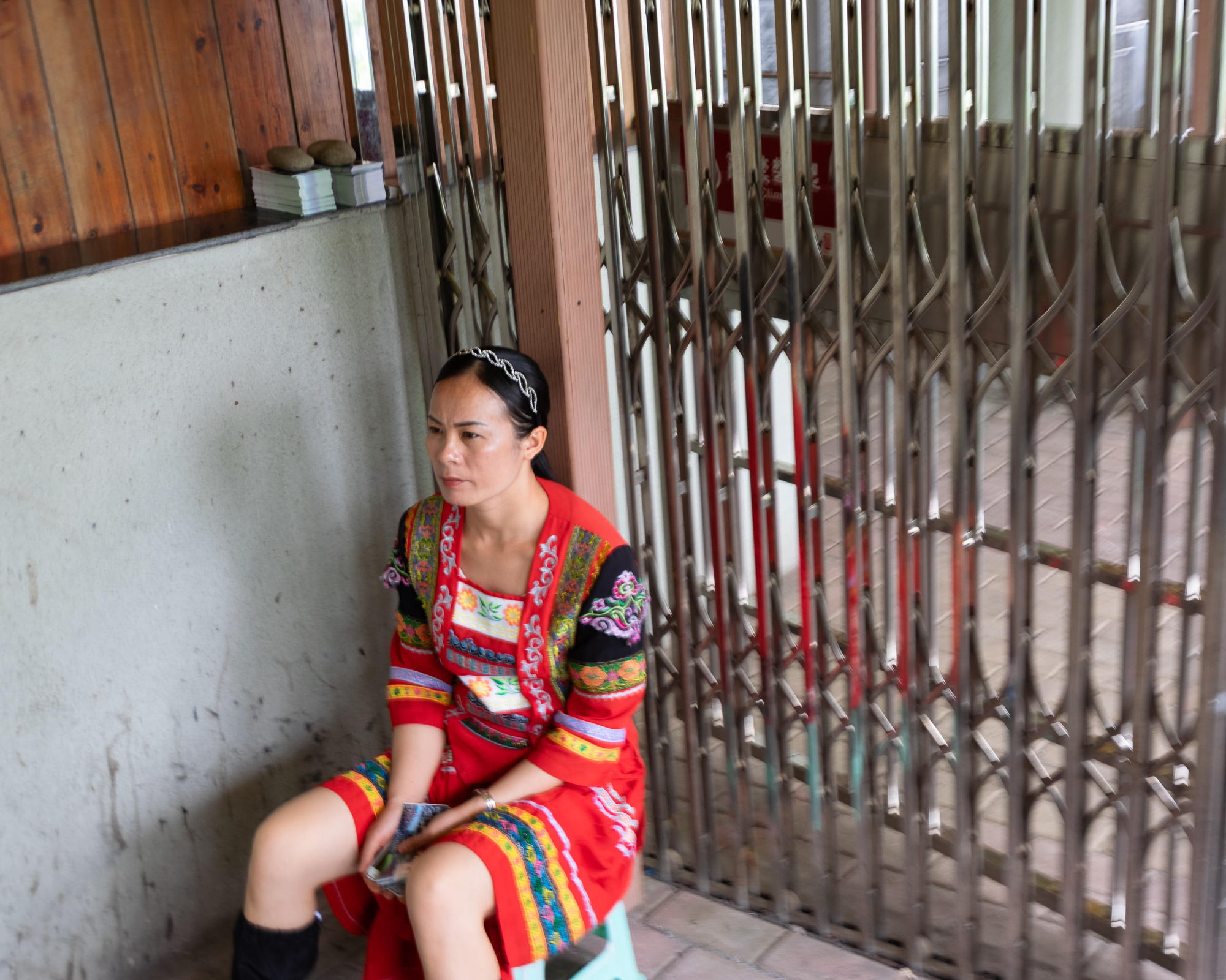 Woman in an embroidered red dress beside a metal gate, Yangshuo China