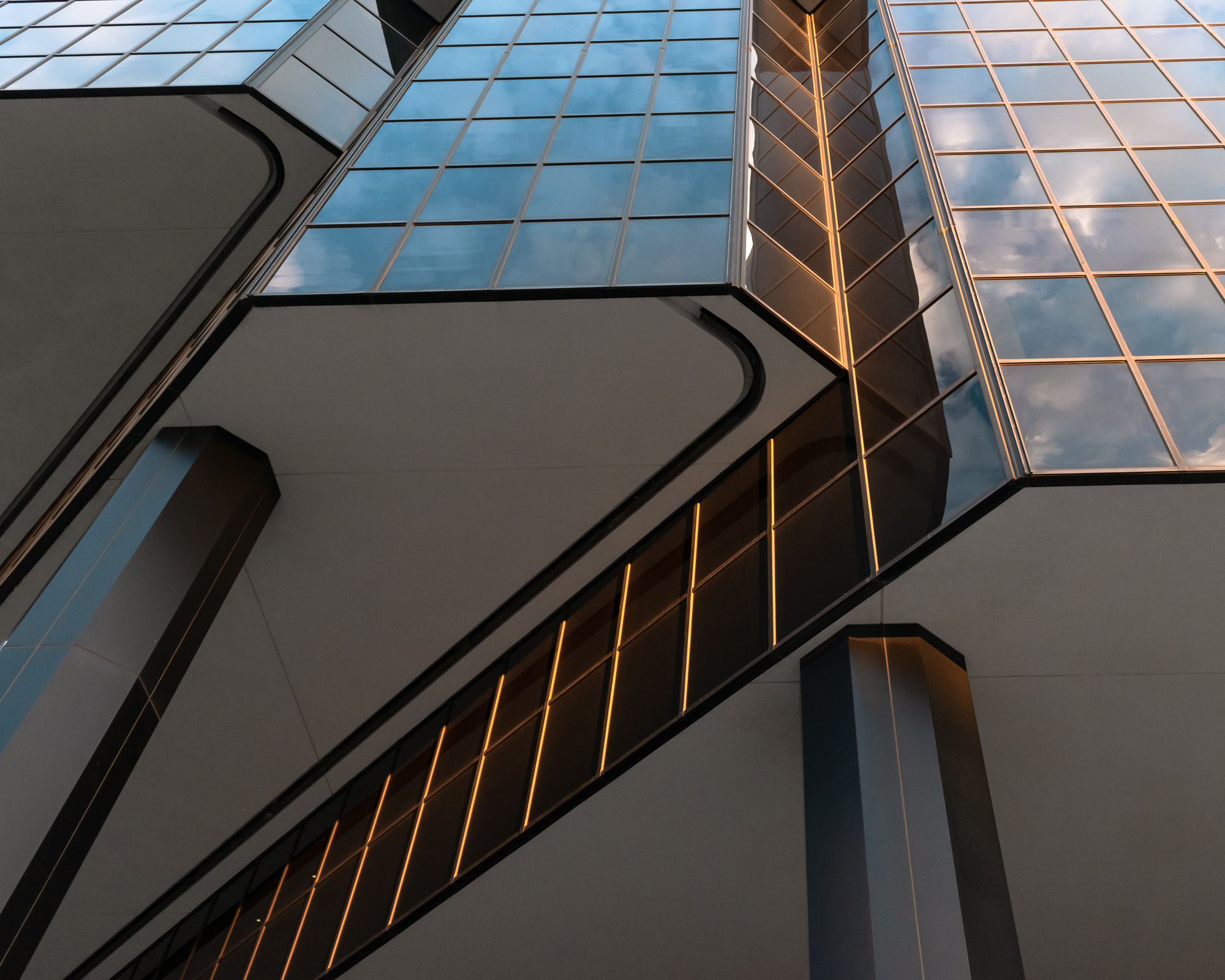 Looking up at Denver glass and steel towers from below — dramatic upward perspective, golden light in the seams, sky reflected in the glass — digital