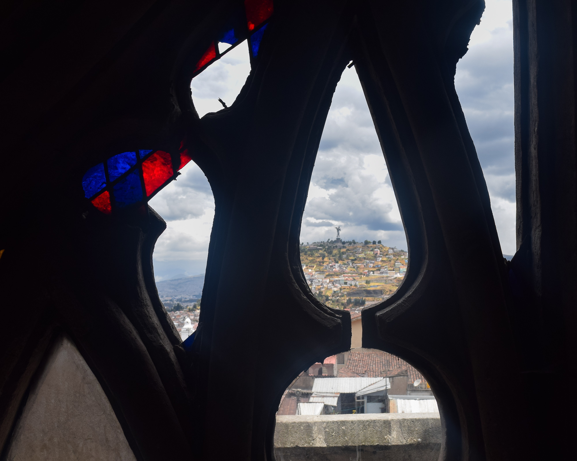 A solitary man sits on a cobblestone hill street in Quito, colorful colonial buildings receding behind him