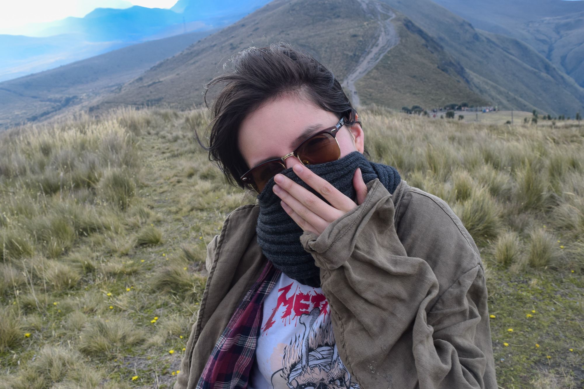 A figure climbing the grassy páramo path, back to camera, wind in hair, pale sky above