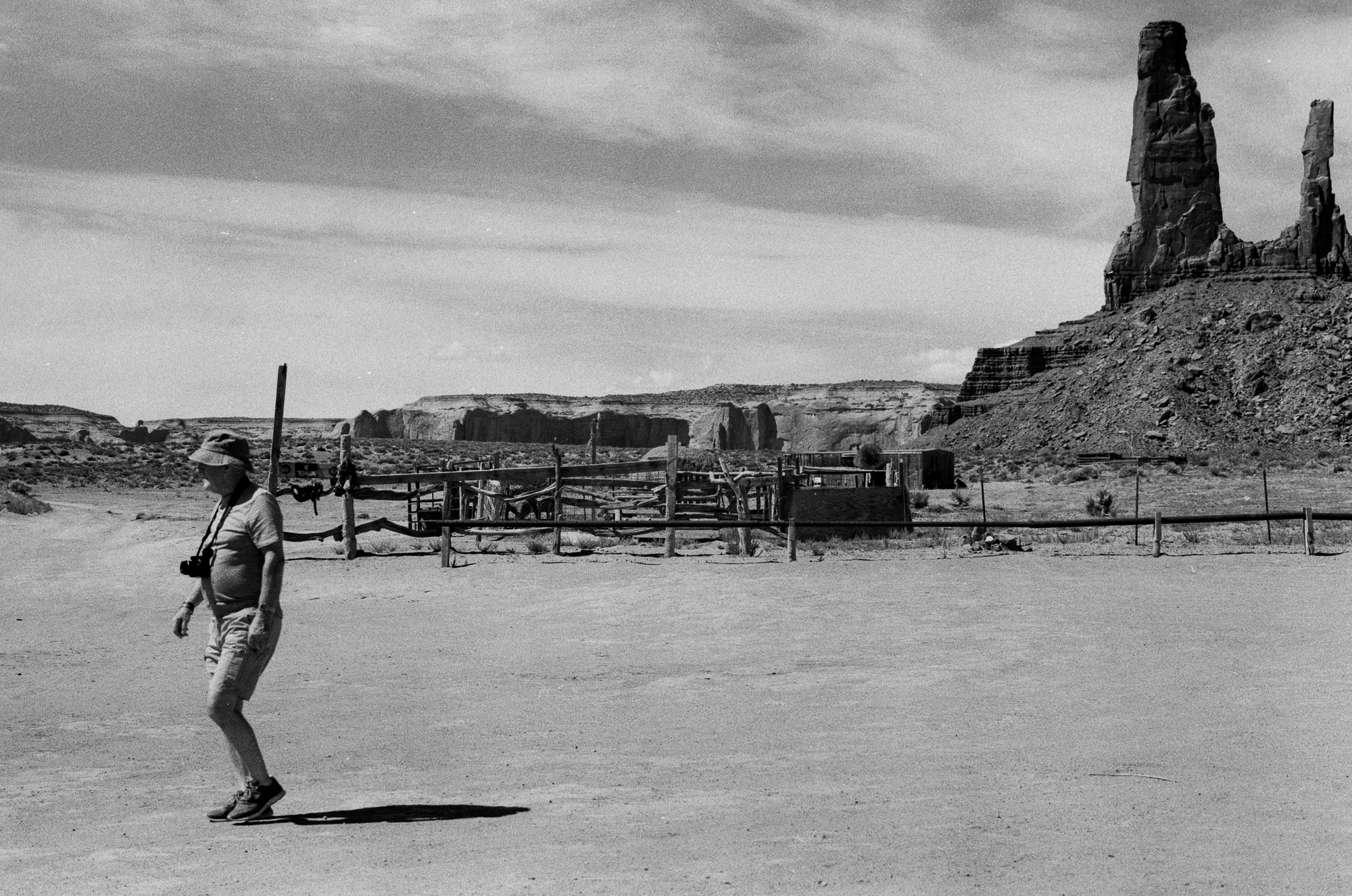 Tourist with camera walking past a corral at Monument Valley, 35mm analog black and white