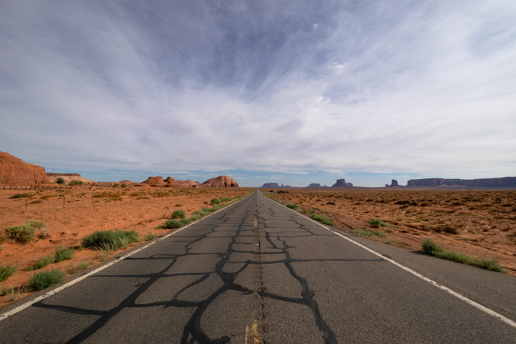 A barren two-lane road stretches to the desert horizon under a vast Arizona sky — no cars, no sign of movement