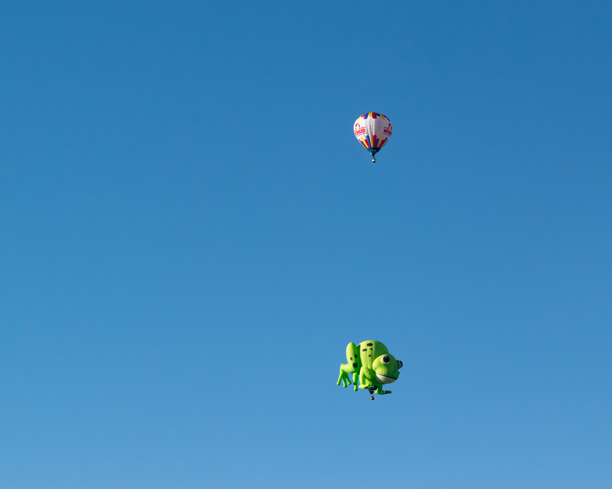 A bright red hot air balloon rises over Colorado, a smiling figure visible in the basket below a wide blue sky