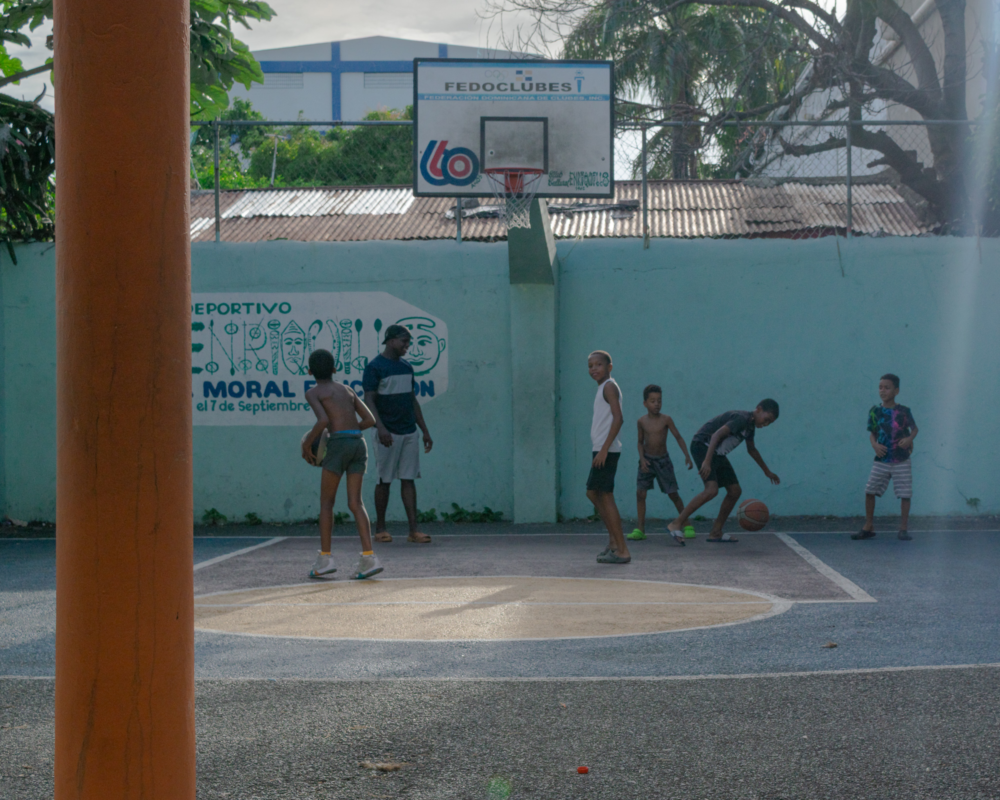 Kids playing basketball in a Santo Domingo park — open energy, joy, the only burst of brightness after the rain