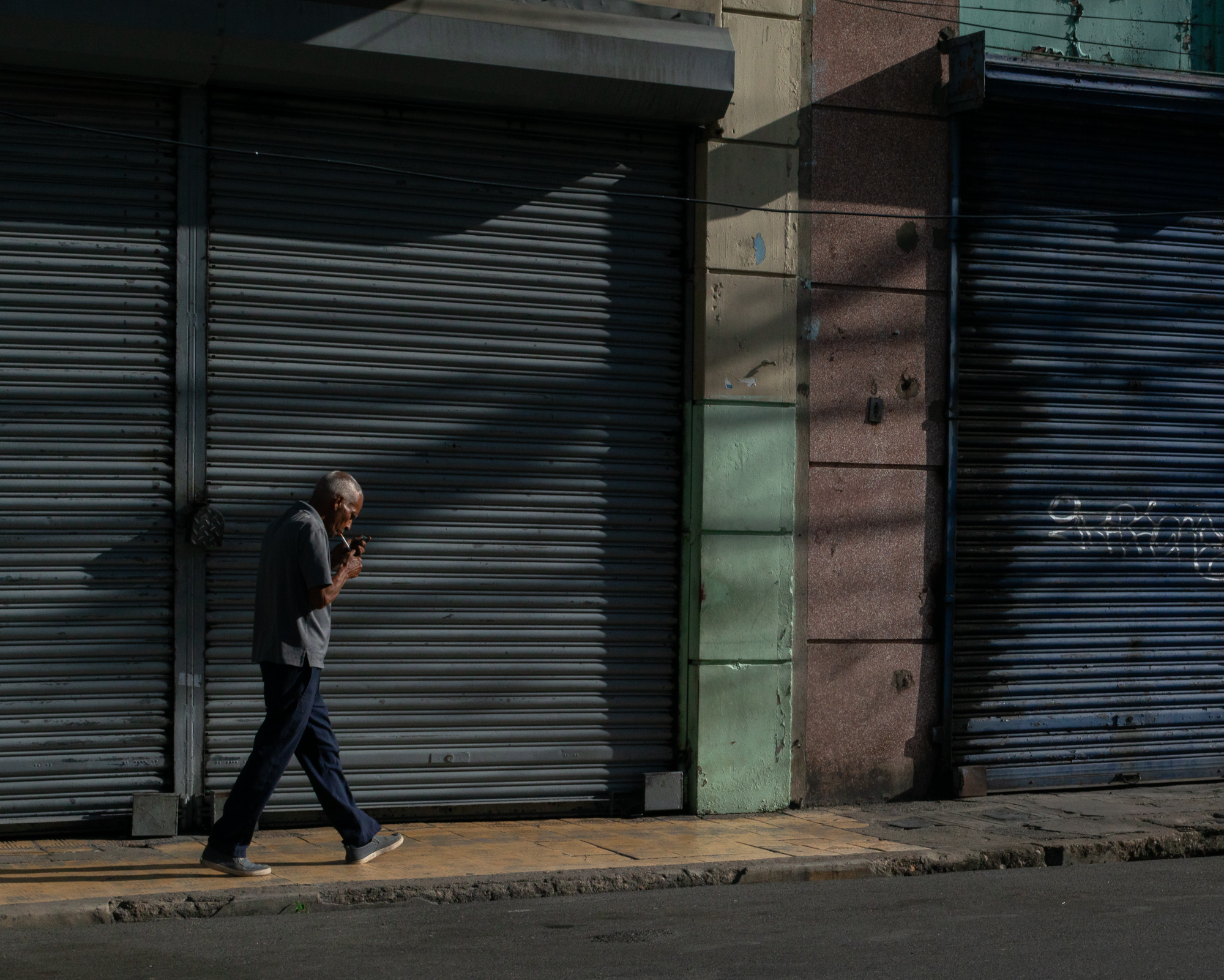 A figure walking through light and shadow in Santo Domingo — geometry, color, street