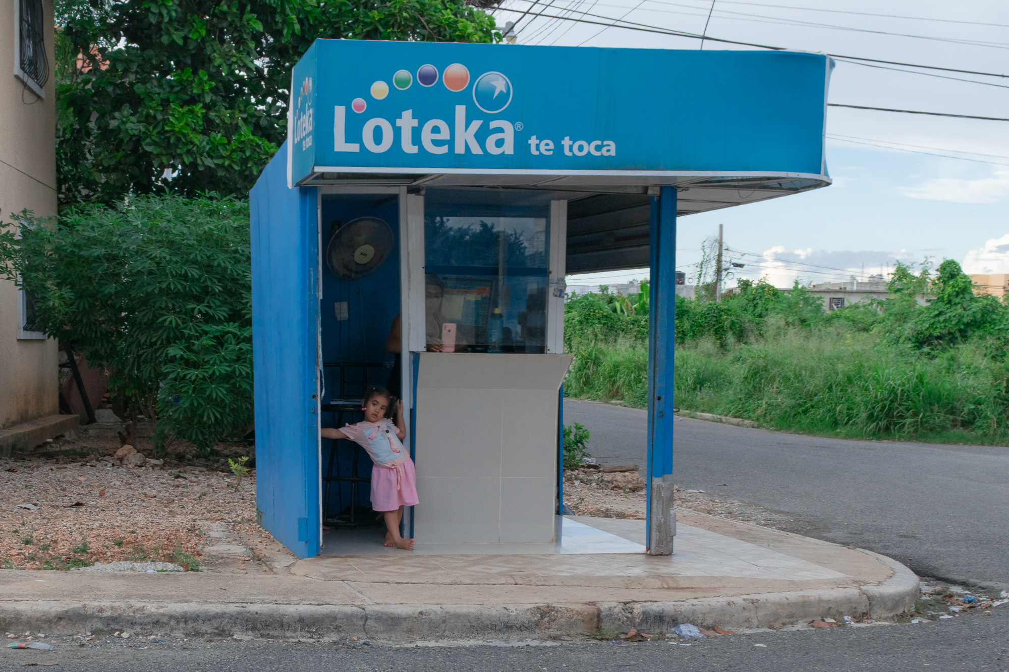 A child alone at a Loteka lottery kiosk in Santo Domingo — solitary, innocent