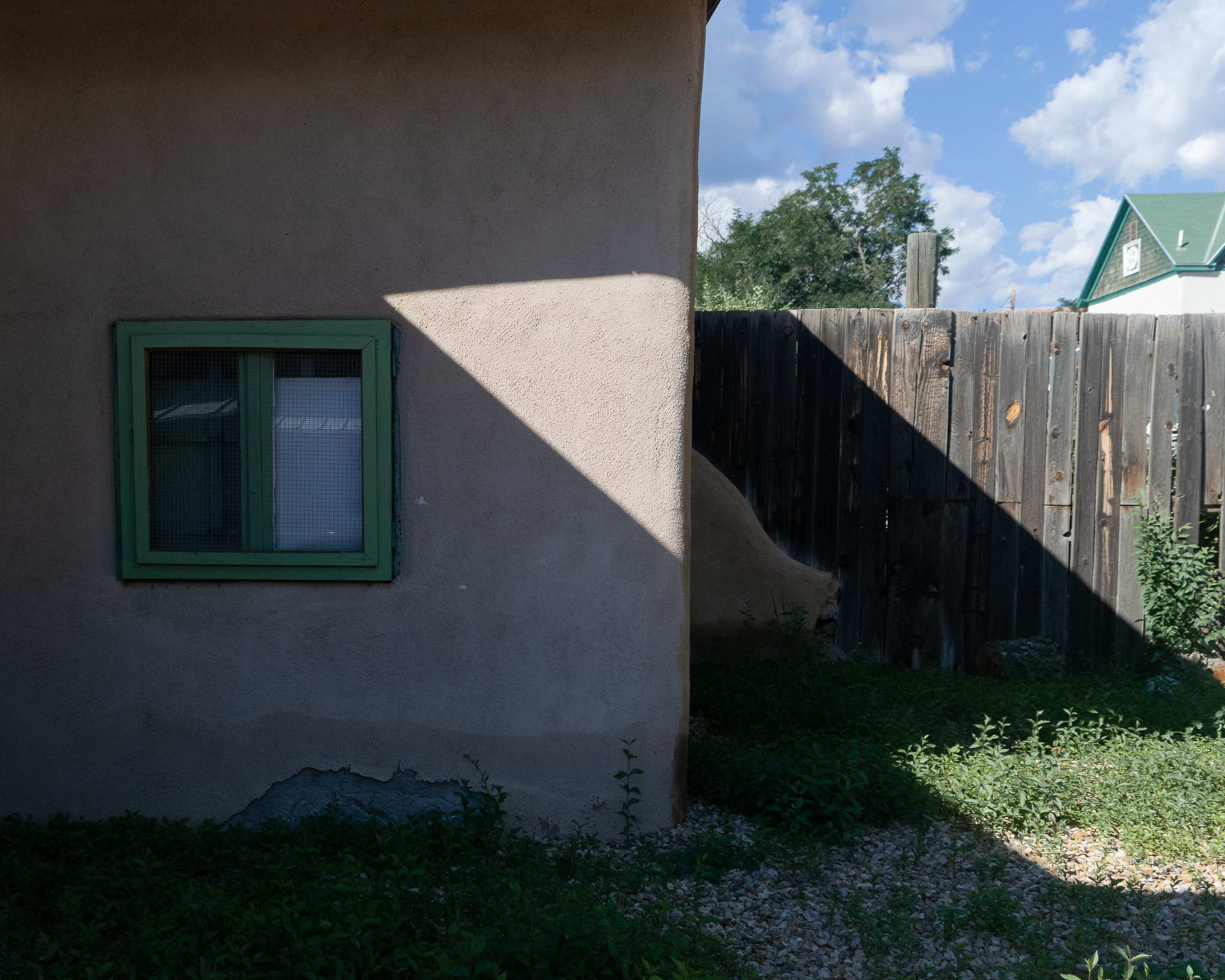 Light and shadow on an adobe wall in a Santa Fe backyard — clean geometric shadow lines across warm terracotta