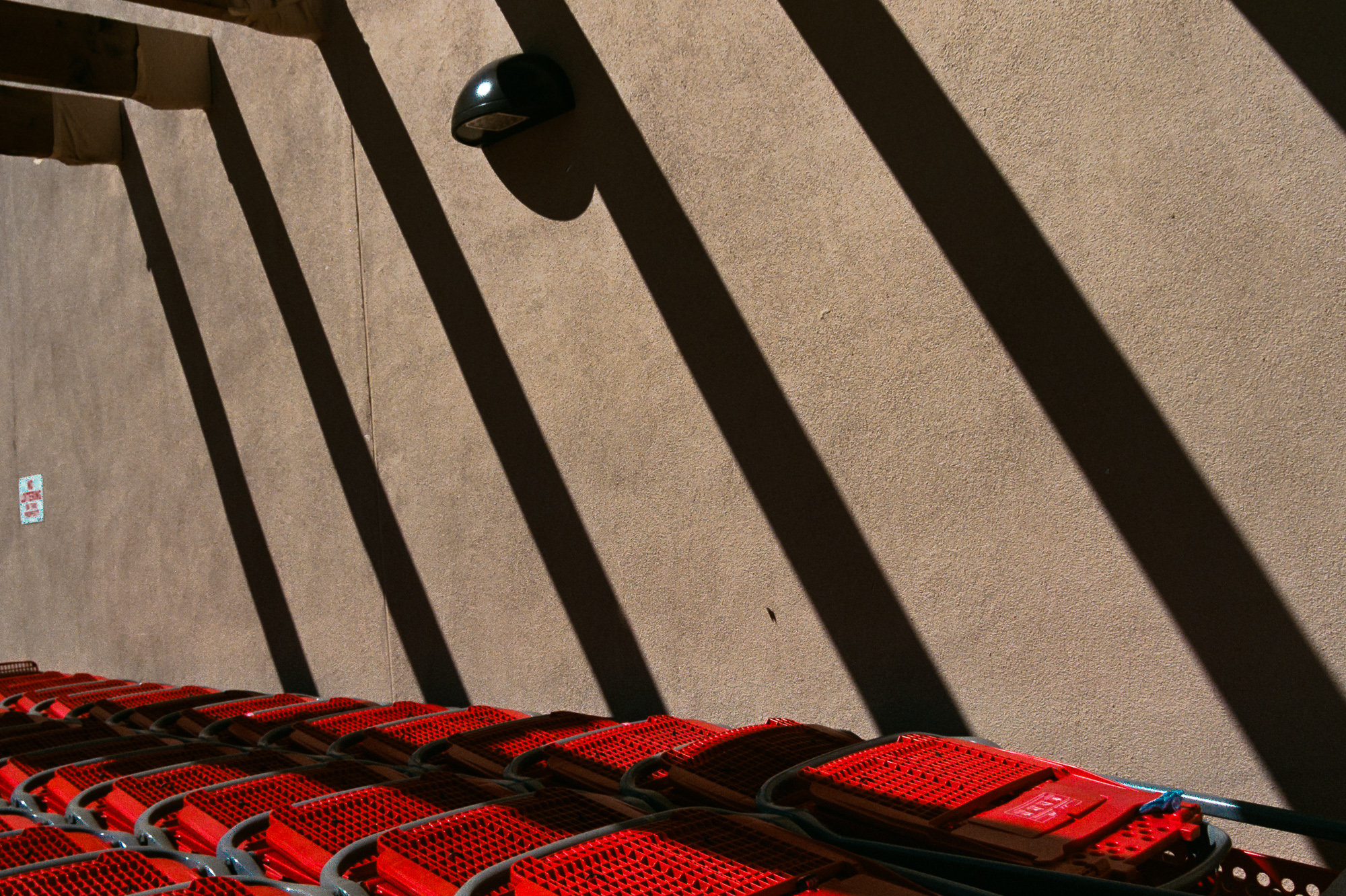 Shopping carts casting shadows on a sidewalk in Santa Fe, a red fire door sign in the background