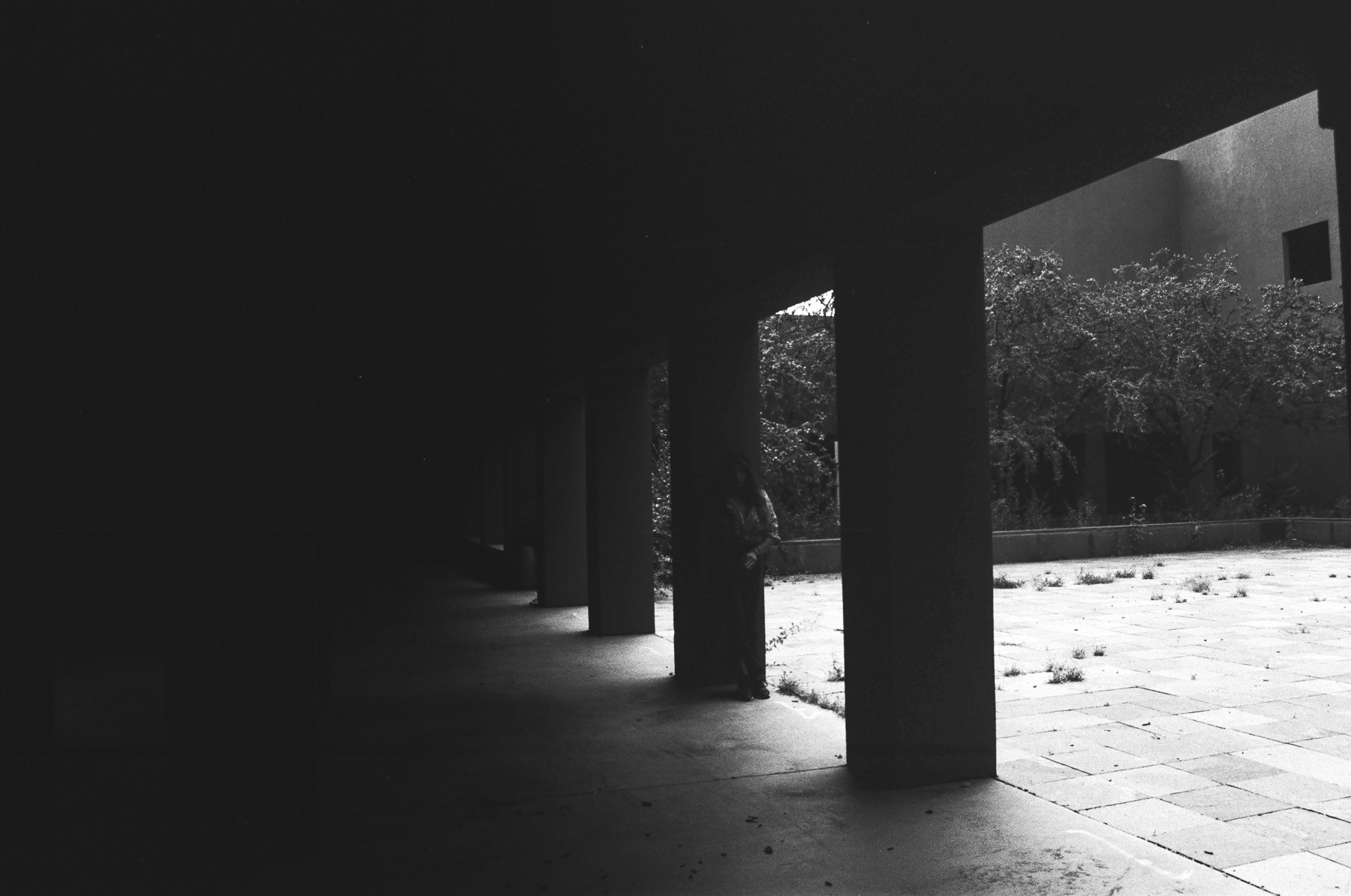 An obscured scene in Santa Fe — a figure between columns in shadow making the subject difficult to read, analog color 35mm film