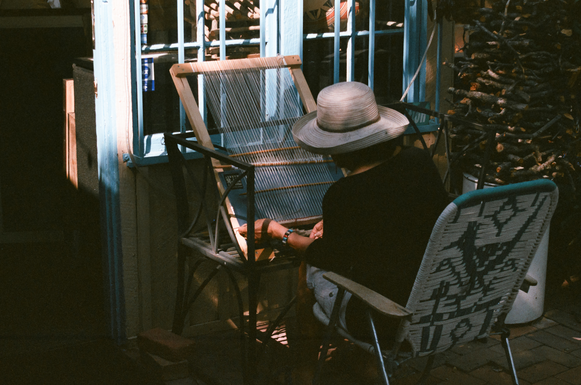A weaving loom casting a geometric shadow pattern on an adobe wall, an artist at work in Santa Fe — color 35mm film