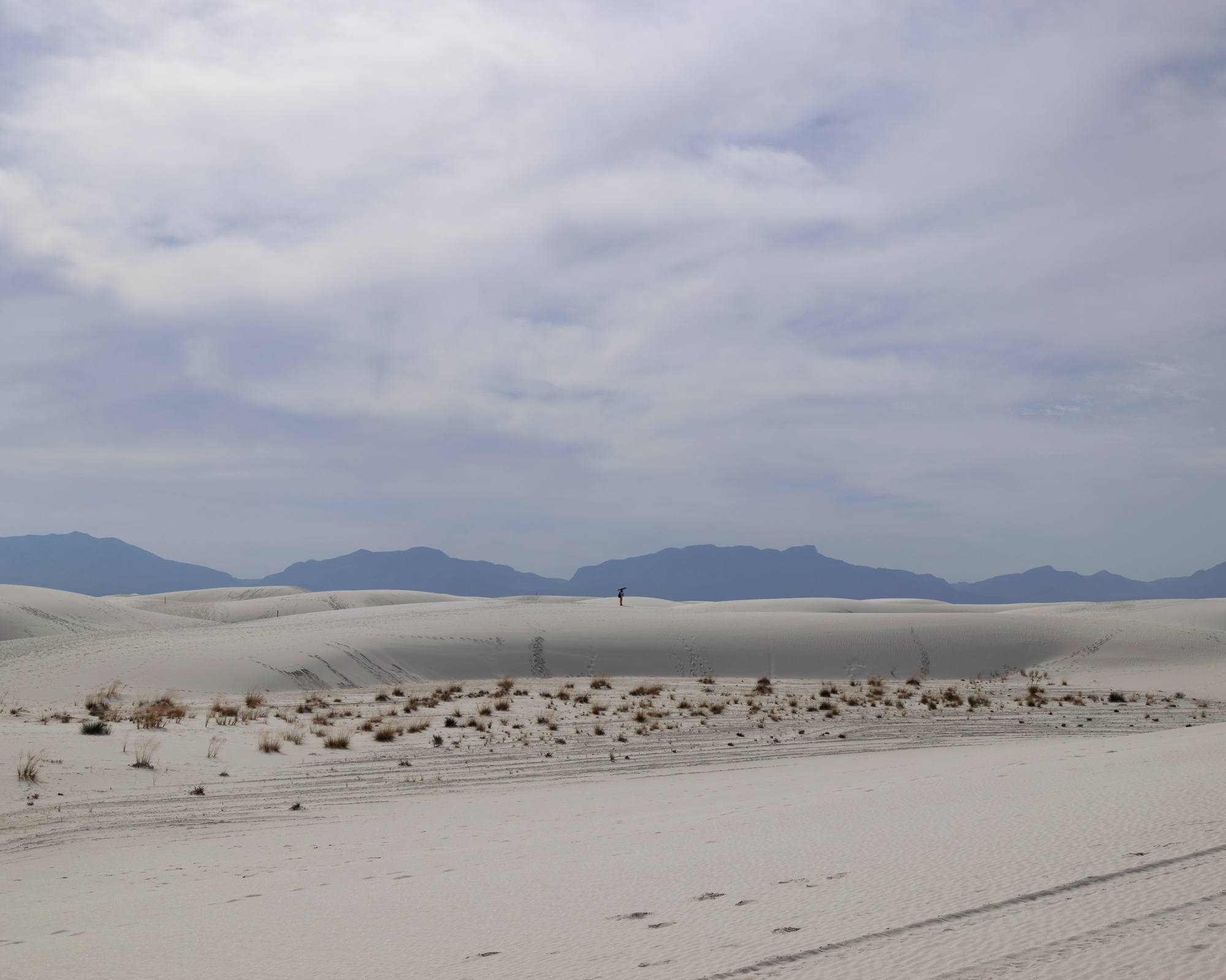 Lone figure on White Sands dunes beneath a cloudy sky