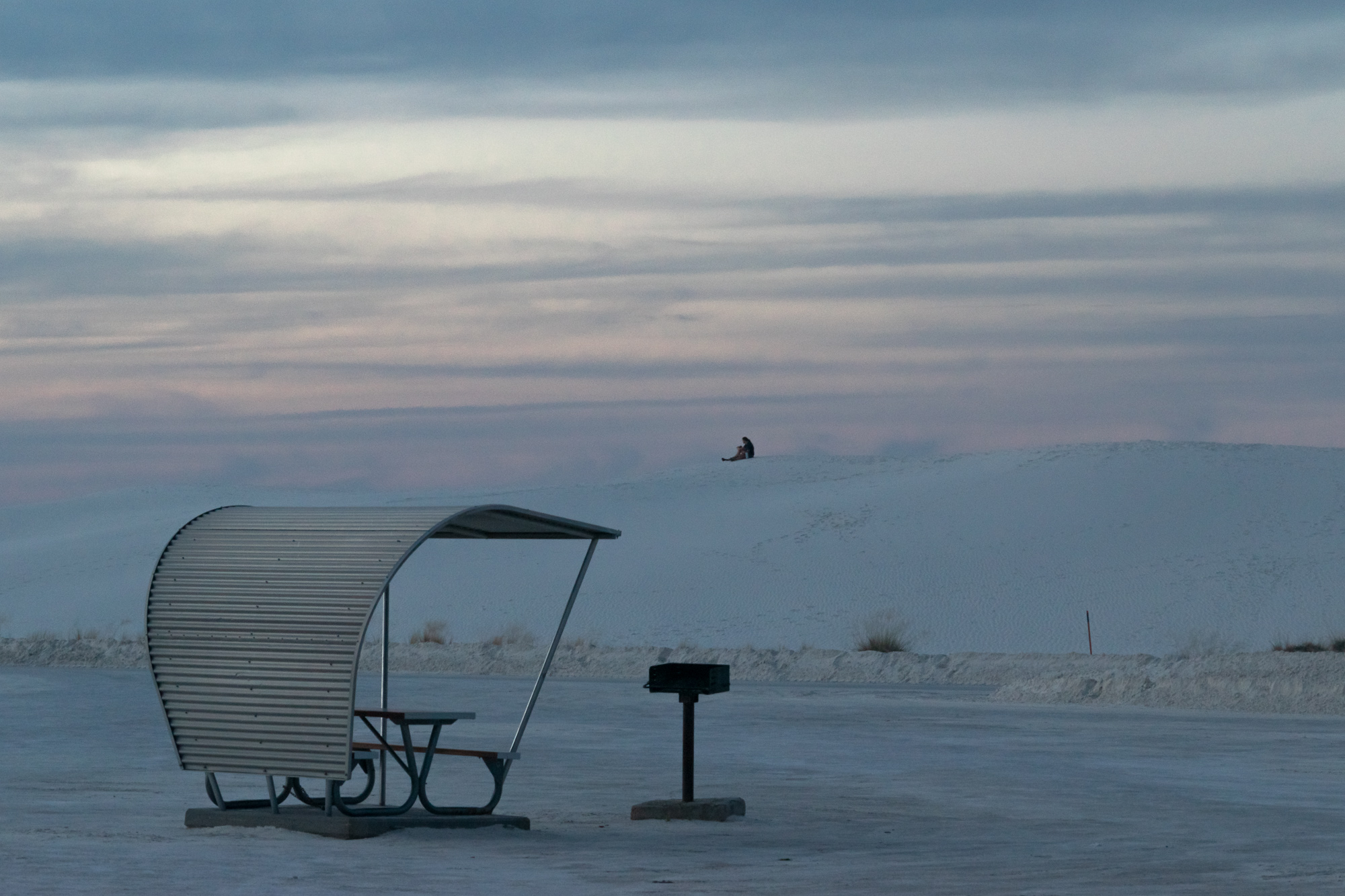 Lone figure on dune above a picnic shelter at dusk, White Sands
