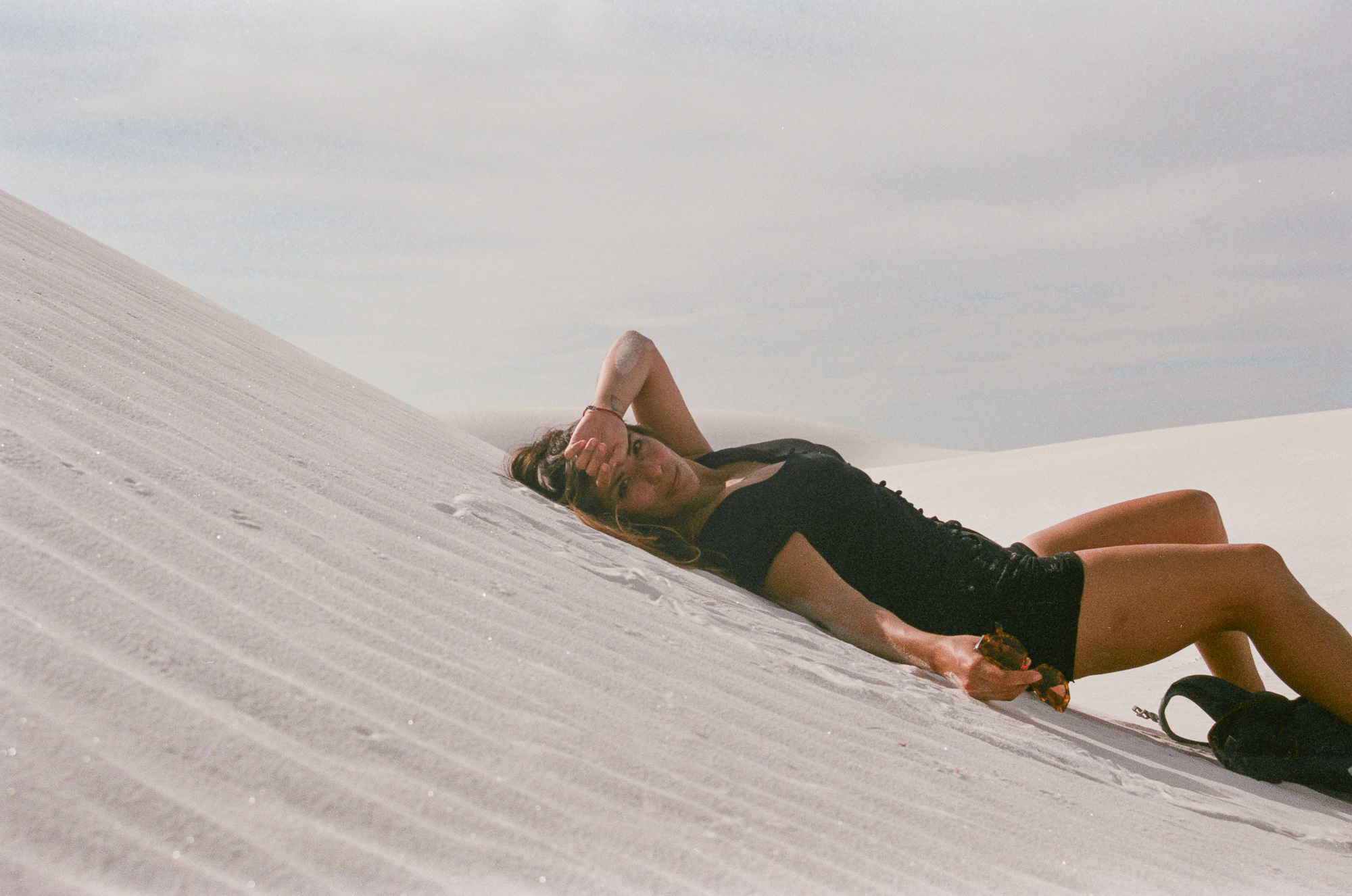 Woman reclining on White Sands dune in a black dress, 35mm film
