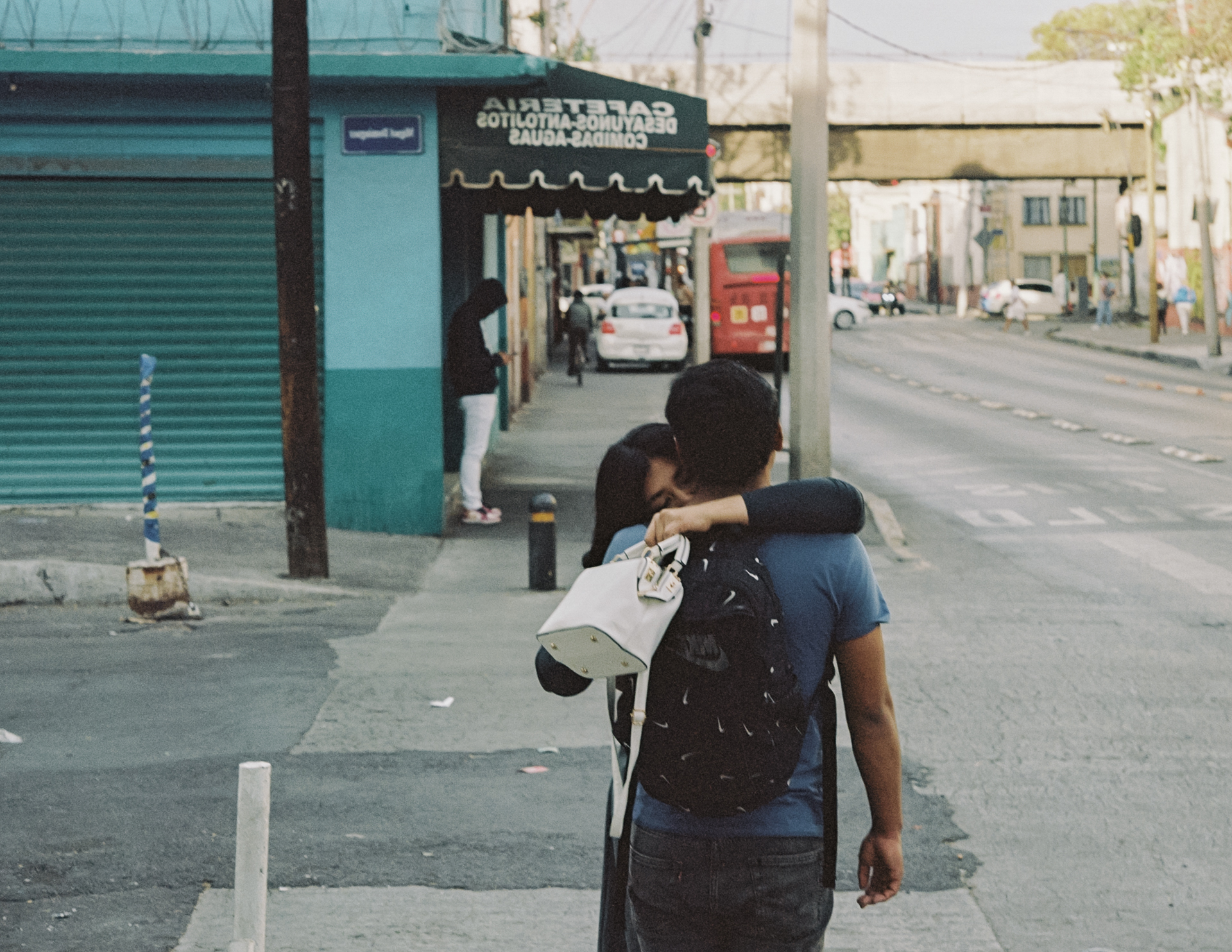 Two people embrace on a sidewalk corner in Mexico City